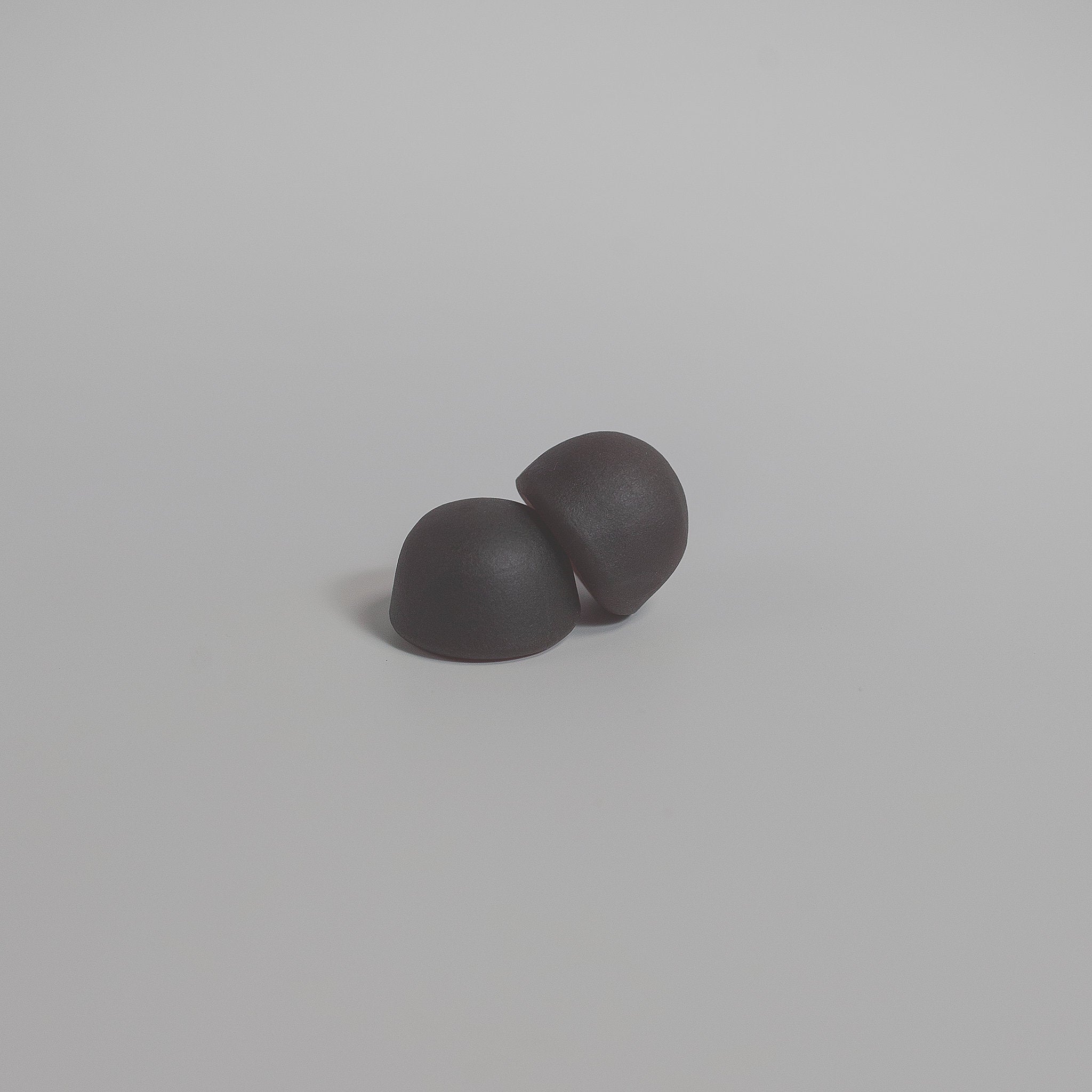 Two black hemispherical supplement gummies on a light gray background